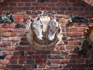 Rzeźba dwóch końskich głów na tle ceglanej ściany